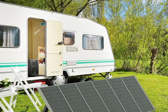 Panneau solaire AFERIY déplié dans l'herbe devant une caravane, relié à la station P210