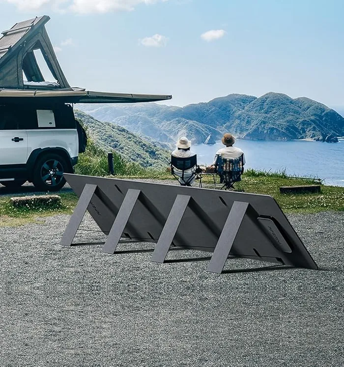 Panneau solaire AFERIY 200W déplié sur ses béquilles face à la mer, un couple assis à l'arrière d'un pick-up