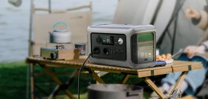 ALLPOWERS R600 posée sur une table de camping au bord de l'eau, devant une tente