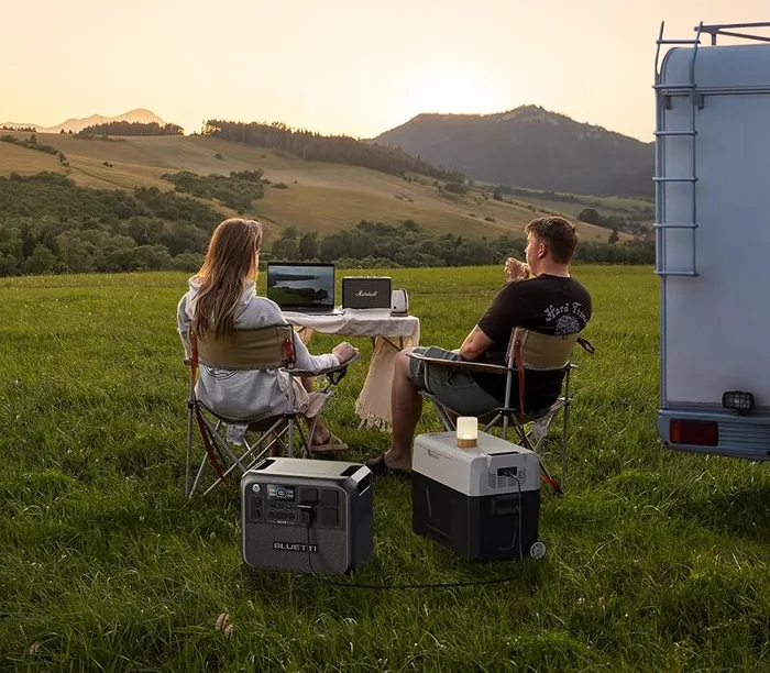 BLUETTI AC200L installée devant une caravane, deux personnes attablées face au coucher de soleil
