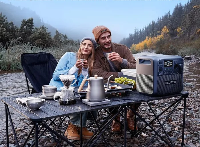 BLUETTI Elite 200 V2 posée près d'une table de camping au bord d'un lac, avec deux personnes attablées