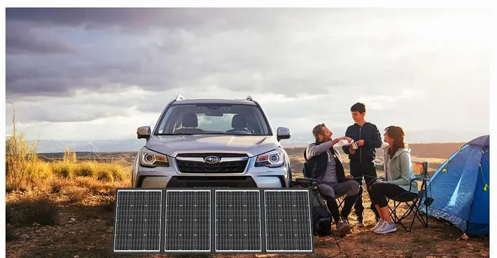 Panneau solaire DOKIO 200W déplié devant un break et une tente, un groupe attablé en arrière-plan
