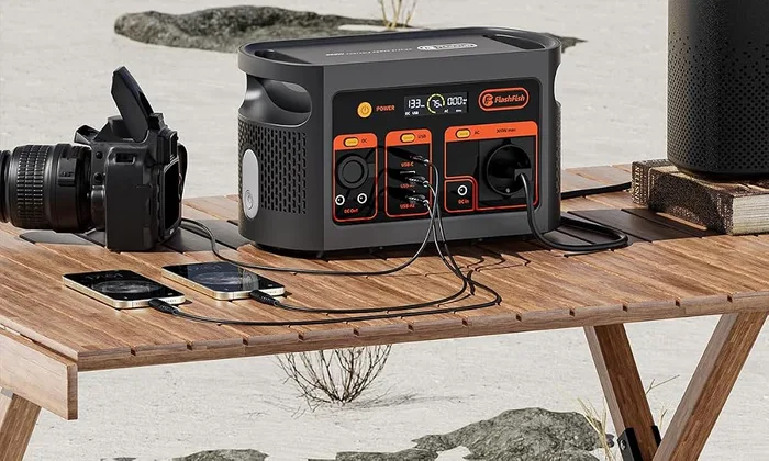 FlashFish E103 sur une table en bois en extérieur, reliée à un appareil photo et à un téléphone