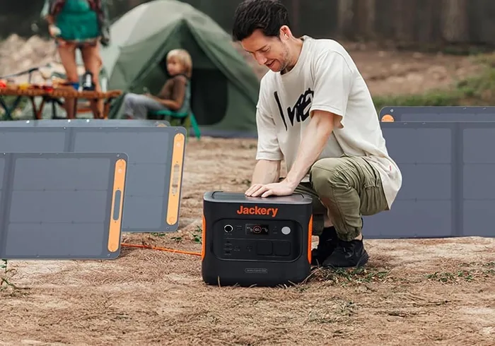 Panneau Jackery SolarSaga 200W installé sur un campement, relié à une station électrique par un utilisateur accroupi