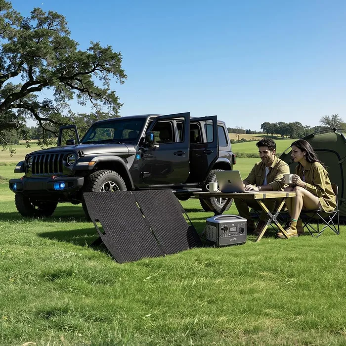 Station VEVOR M6 et son panneau solaire 100 W installés dans un pré devant un 4x4 et une tente